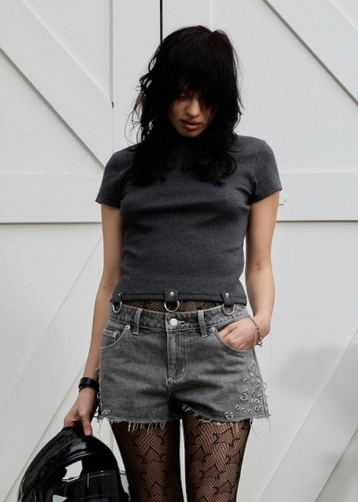 Person wearing a dark gray t-shirt and denim shorts with patterned tights, standing against a white background.