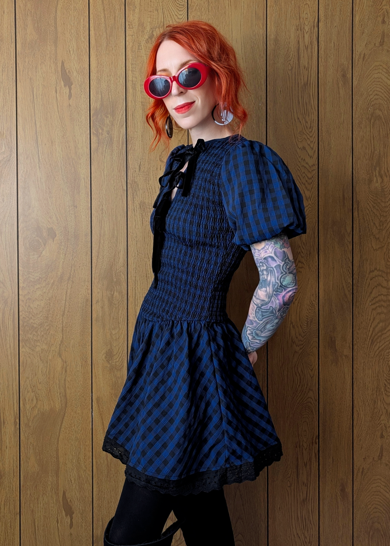 Person wearing a navy and black checkered dress against a wooden wall