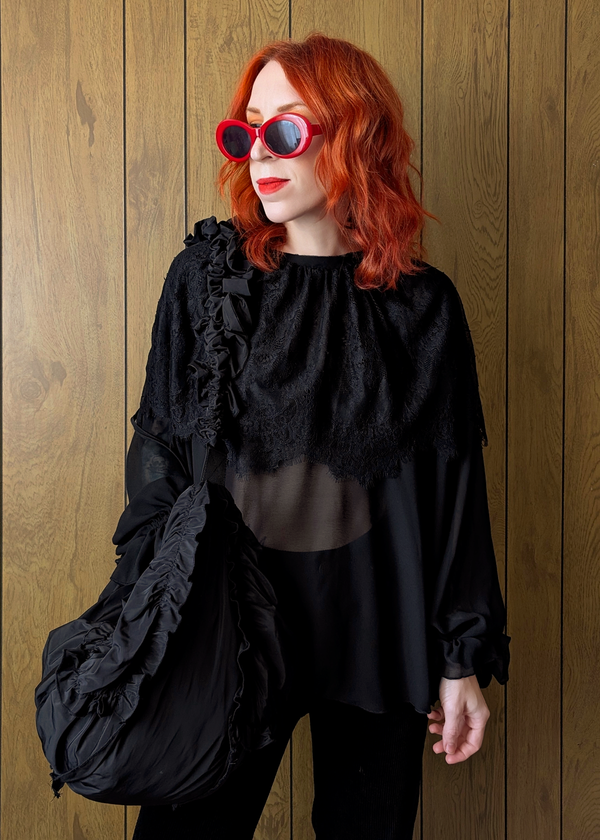 Person wearing a black outfit with ruffled details against a wooden background