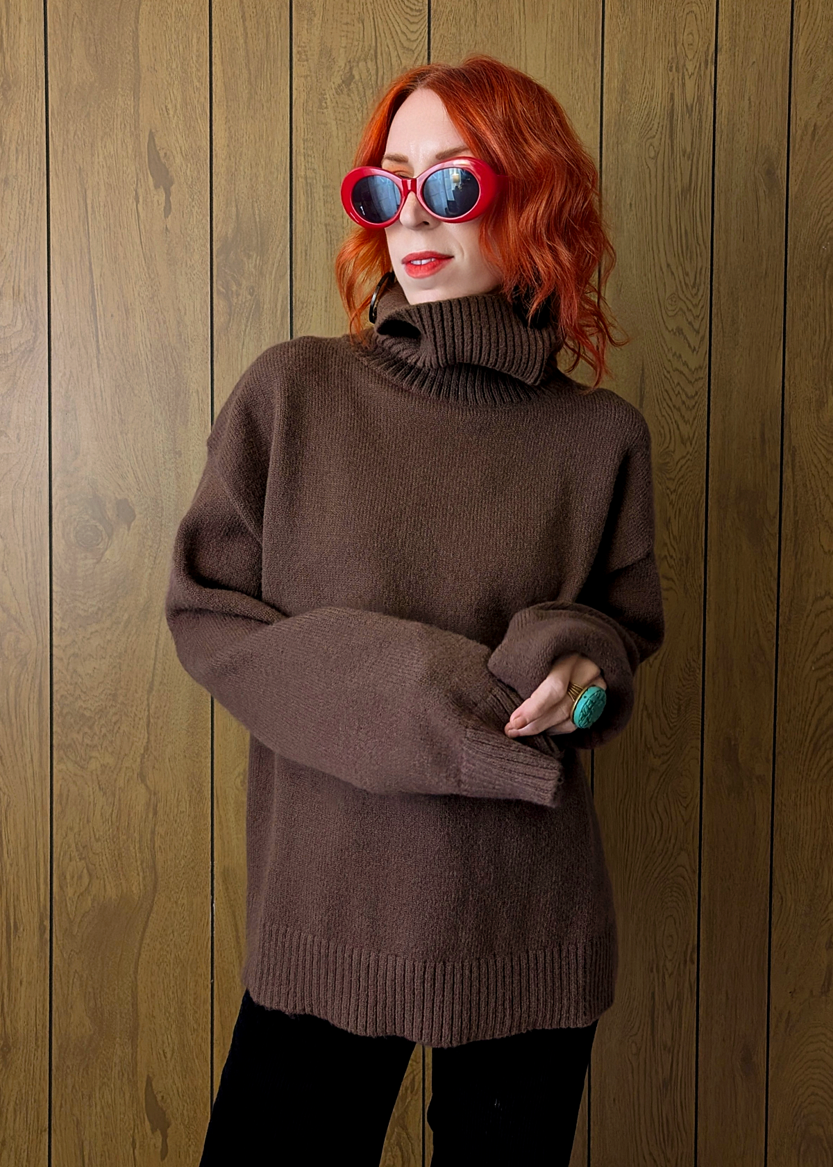 Person wearing a brown sweater and red sunglasses against a wooden background