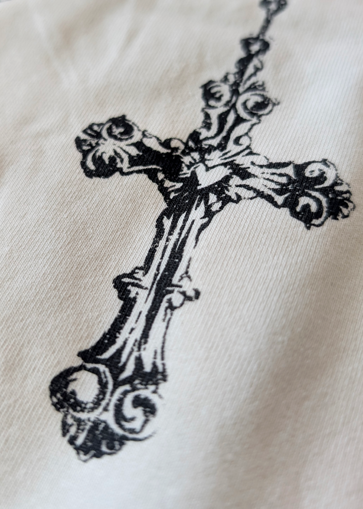 Details of a decorative cross necklace graphic on an ivory t-shirt