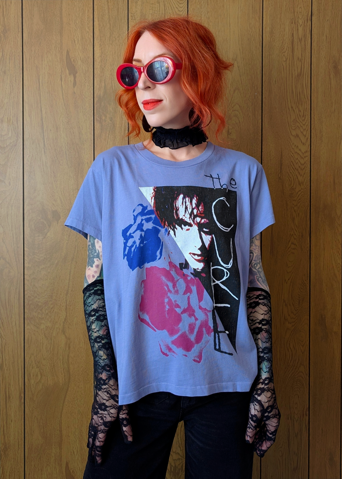 Person wearing a The Cure  t-shirt with graphic design in front of a wooden wall