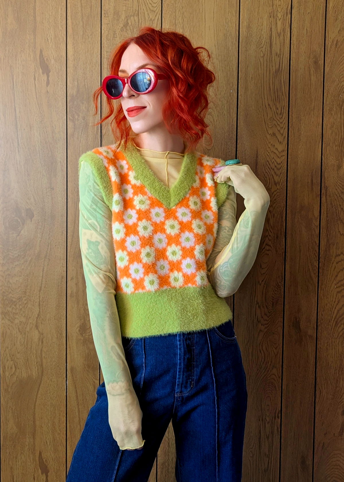 Person wearing a colorful sweater vest with a floral pattern against a wooden background