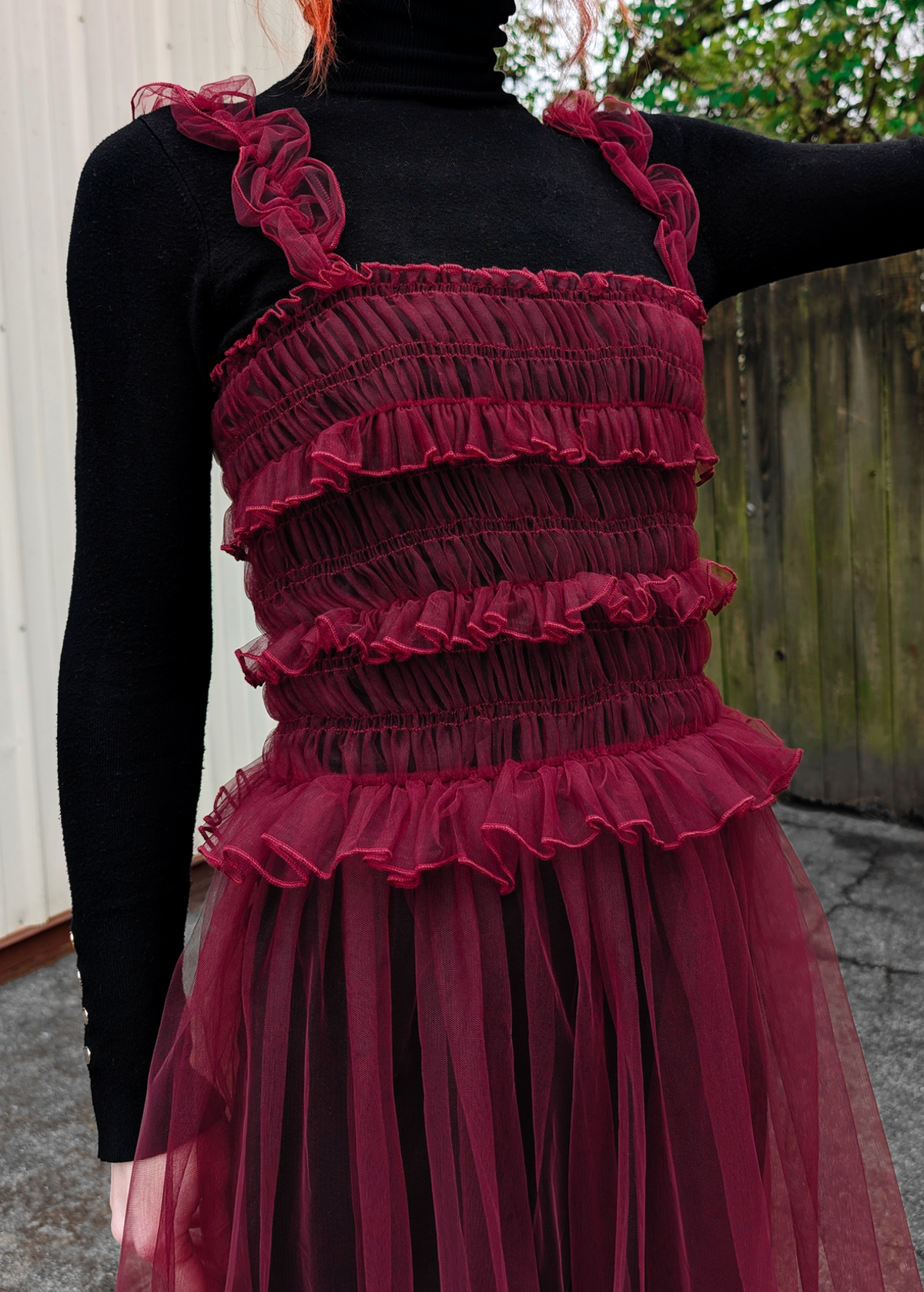 Red ruffled dress with a black long-sleeve top worn by a person, outdoors.