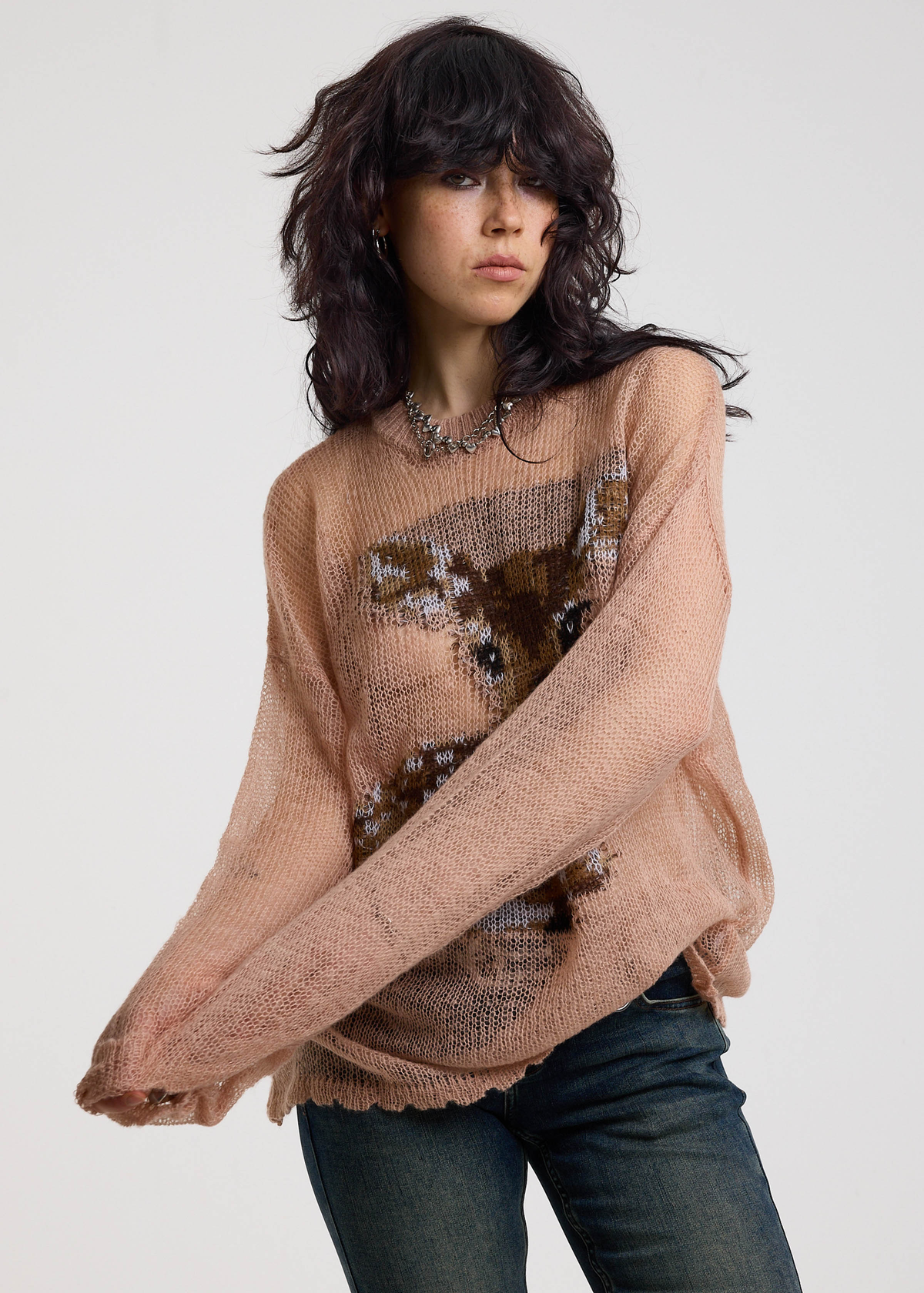 Woman wearing a dusty pink open knit lightweight sweater with a deer design on a plain background