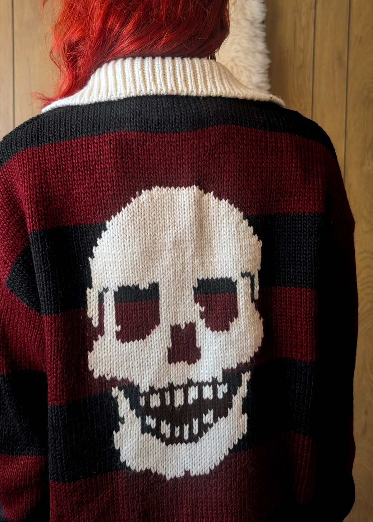 Person wearing a sweater with a skull design, posed against on a wooden background