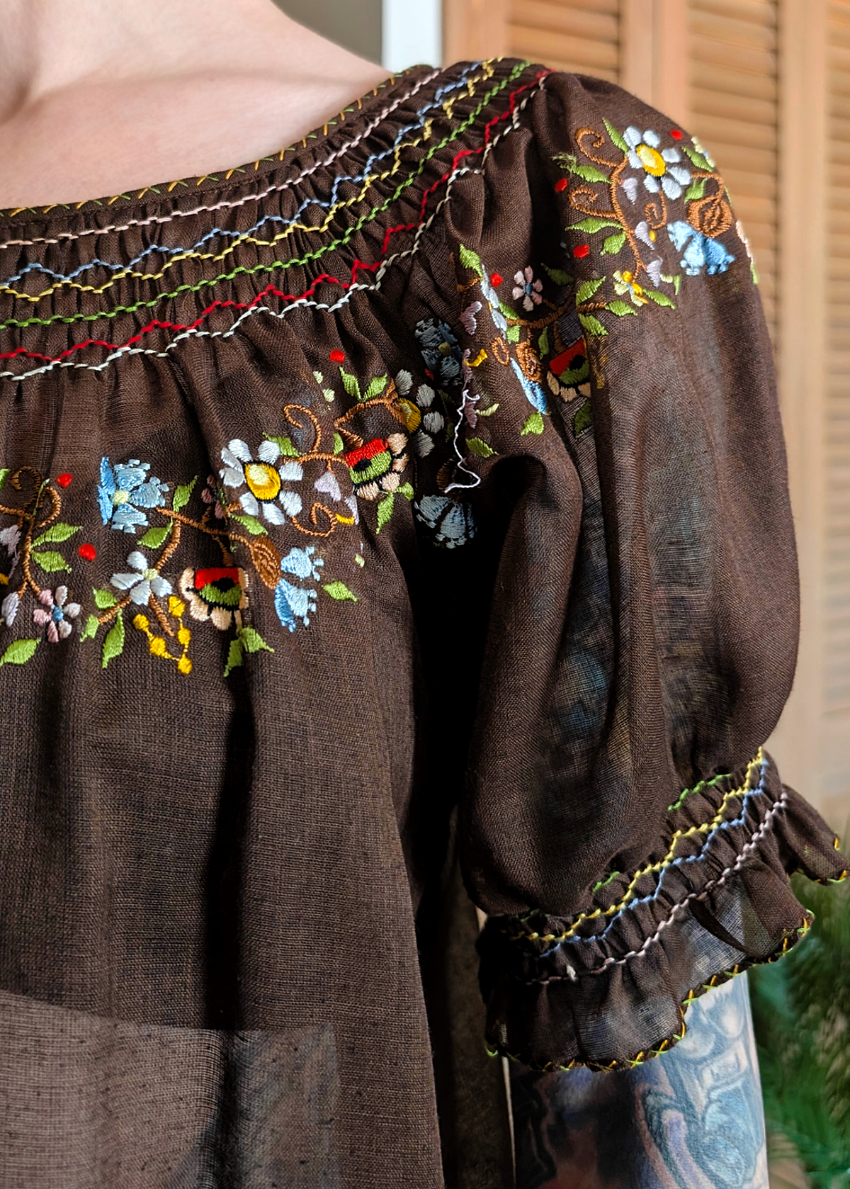 Vintage 1970s gauzy cotton prairie Penny Lane blouse featuring a round neckline, short puff sleeves, and colorful floral embroidery along neckline. Chocolate brown colorway