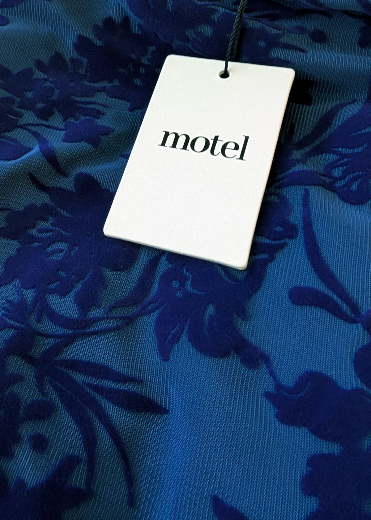 White tag with 'motel' text on a blue floral fabric background