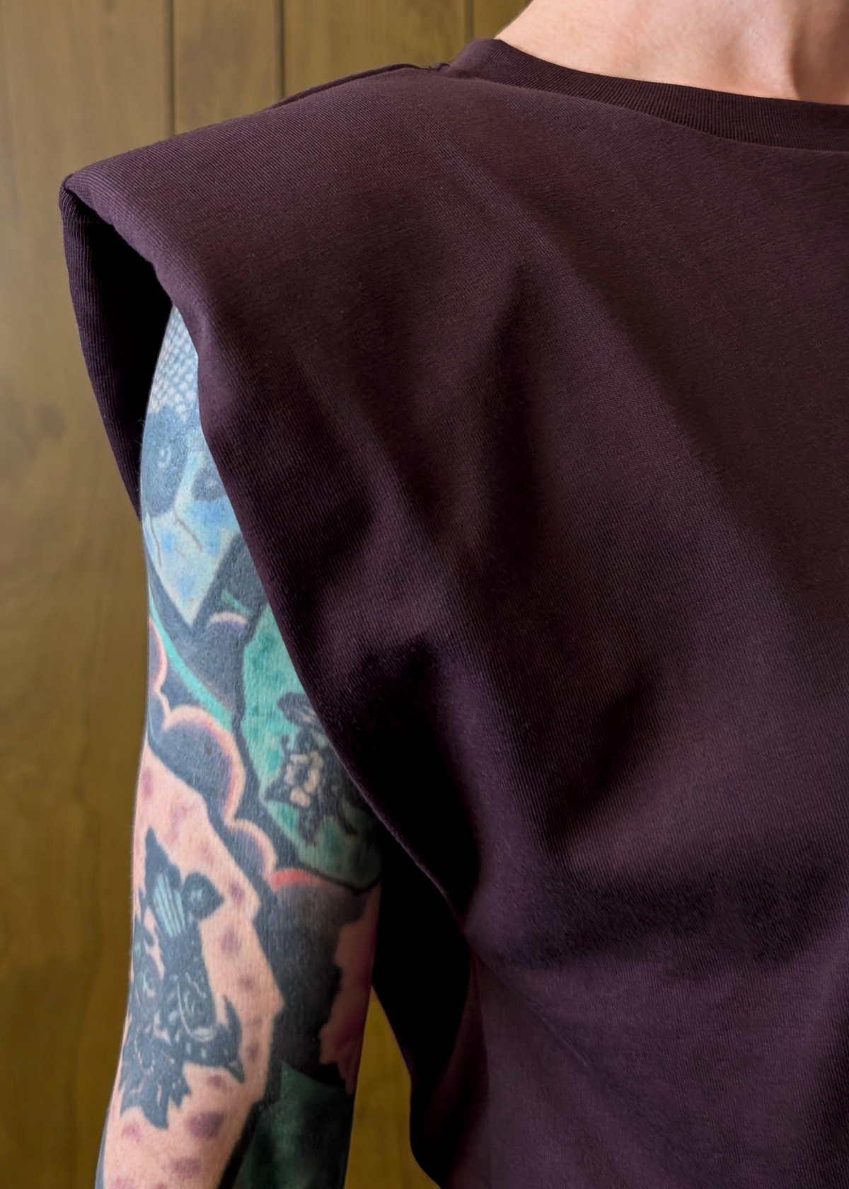 eggplant colored sleeveless top worn by a person with a tattooed arm against a wooden background