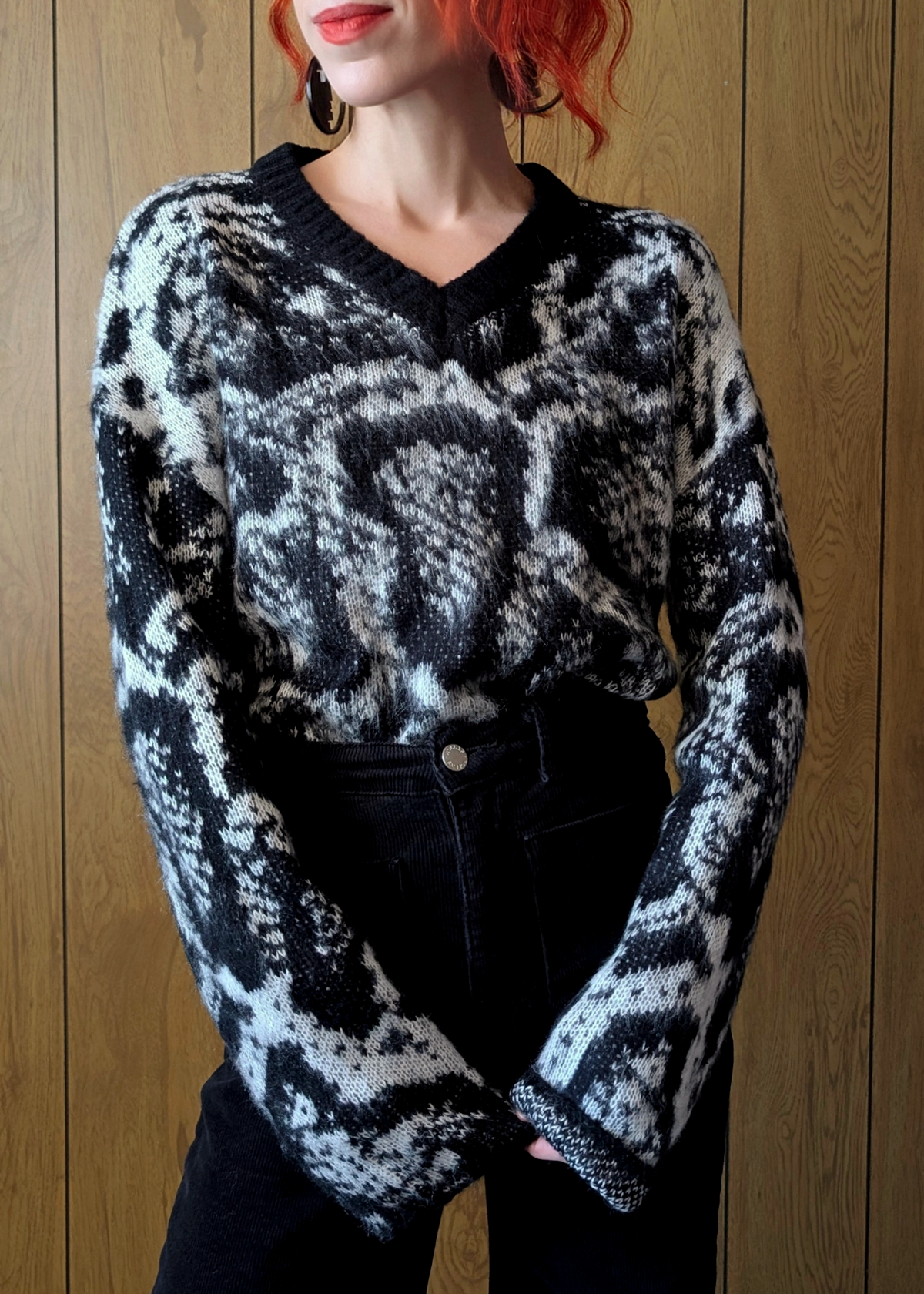 Person wearing a black and white patterned sweater against a wooden background