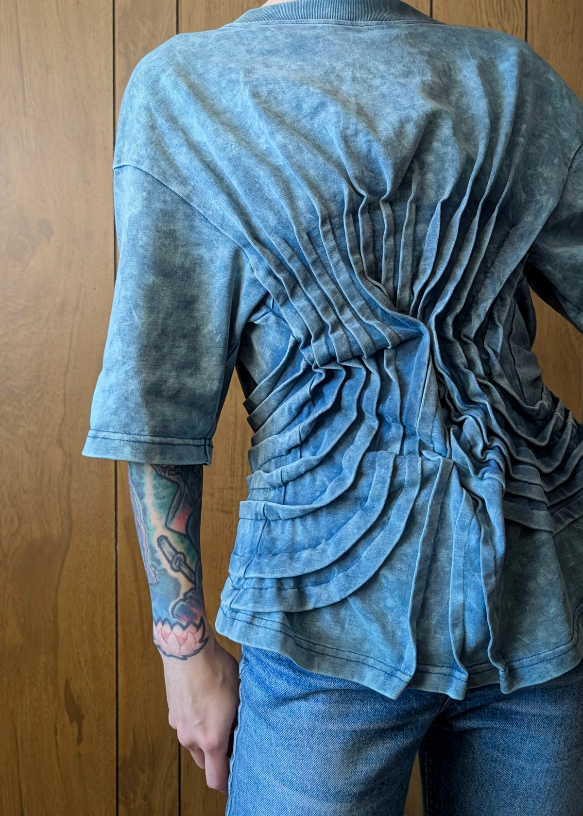 Person wearing a blue ruched top and jeans against a wooden background