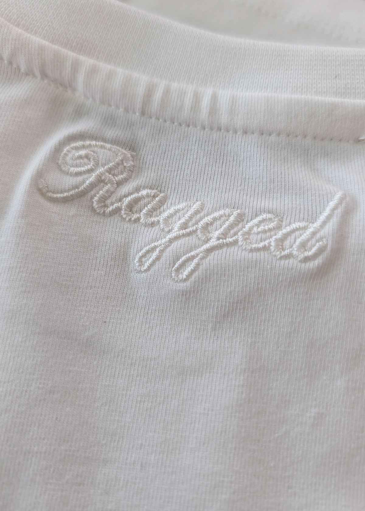 Close-up of an ivory garment with 'Ragged' embroidery in ivory