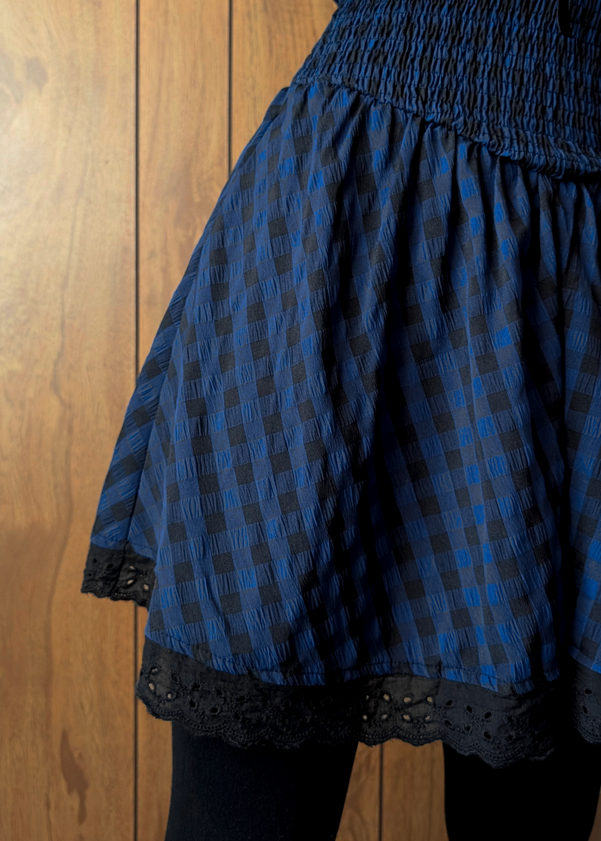 Blue and black checkered dress with eyelet trim on a wooden background