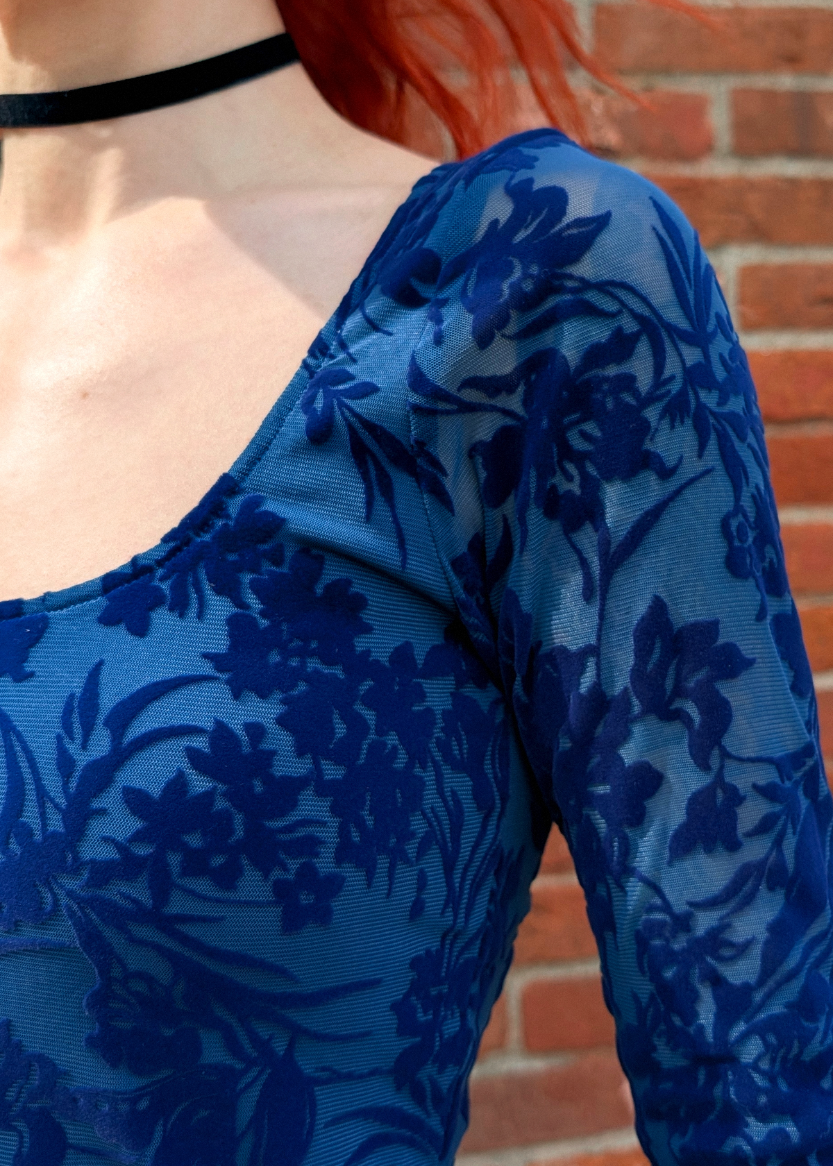 Person wearing a blue floral dress with a brick wall background