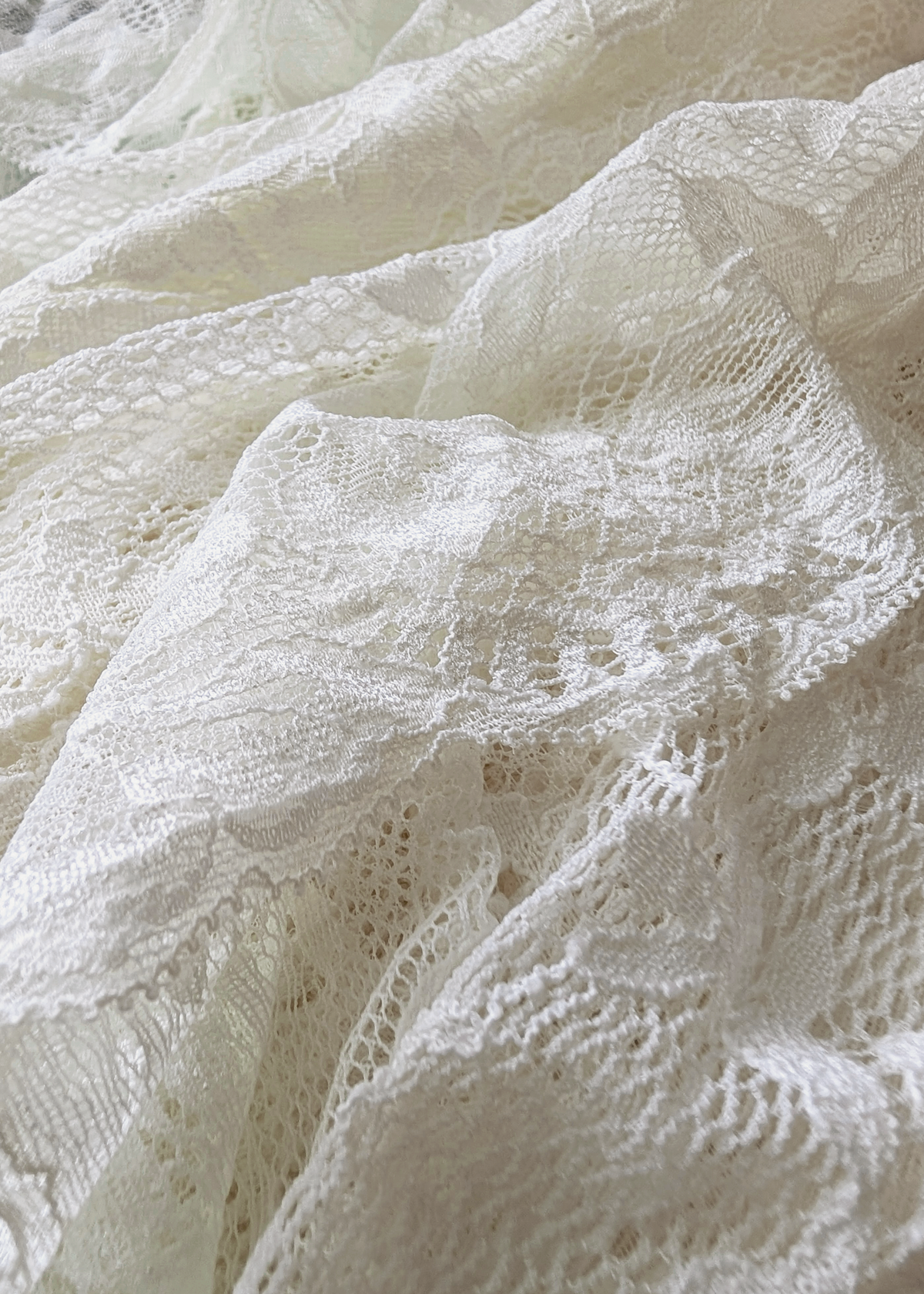 Close-up of draped off-white lace fabric with floral and geometric openwork patterns.