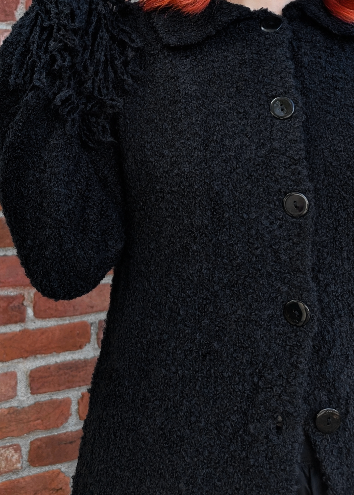texture details of the black cardigan with buttons against a brick wall