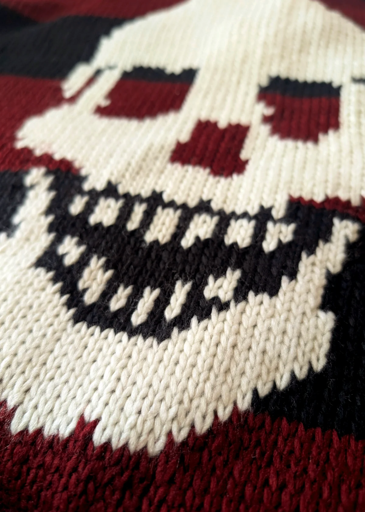 Close-up of a knitted fabric with a skull design in dark red, black, and cream