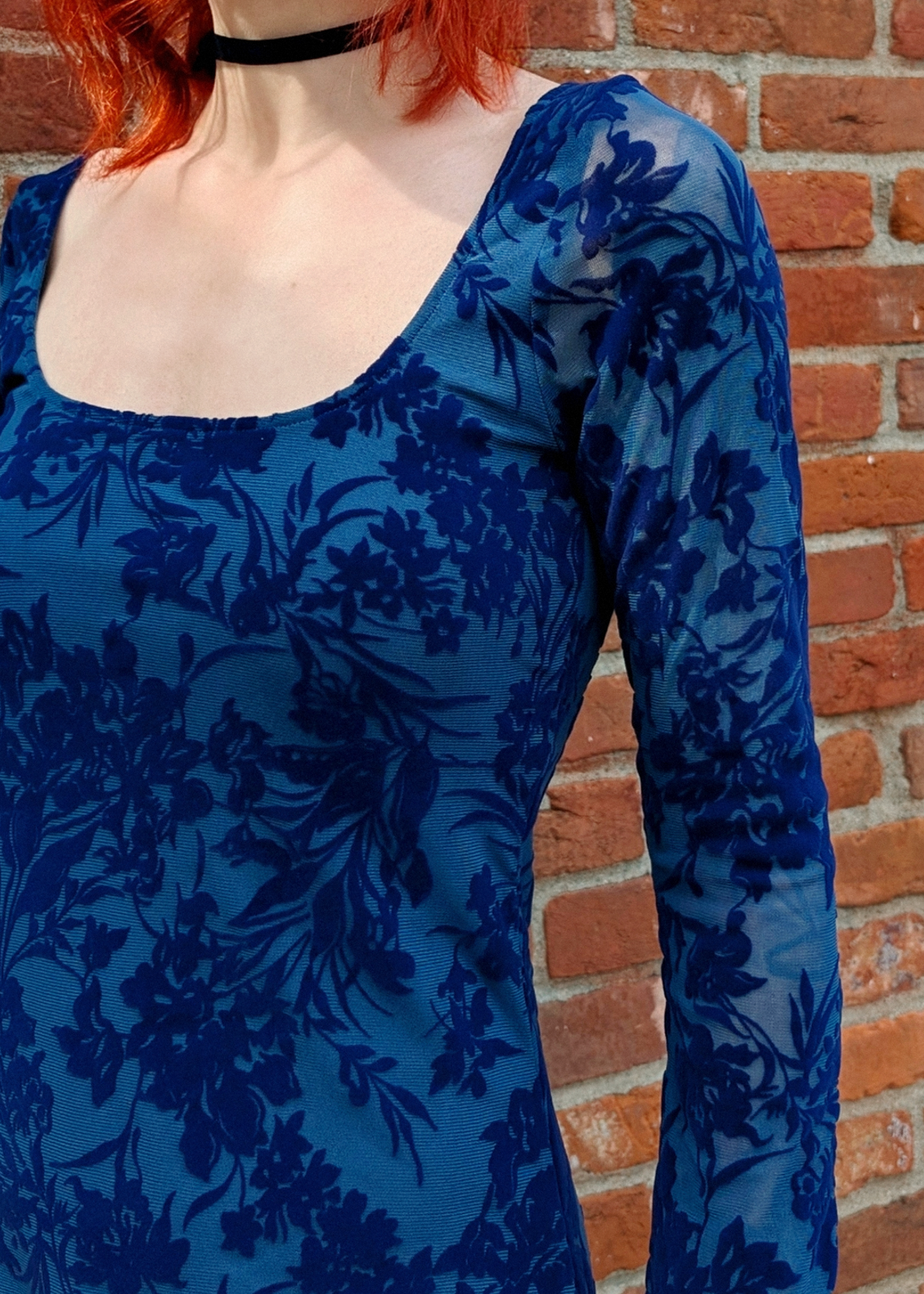 Person wearing a blue floral dress against a brick wall