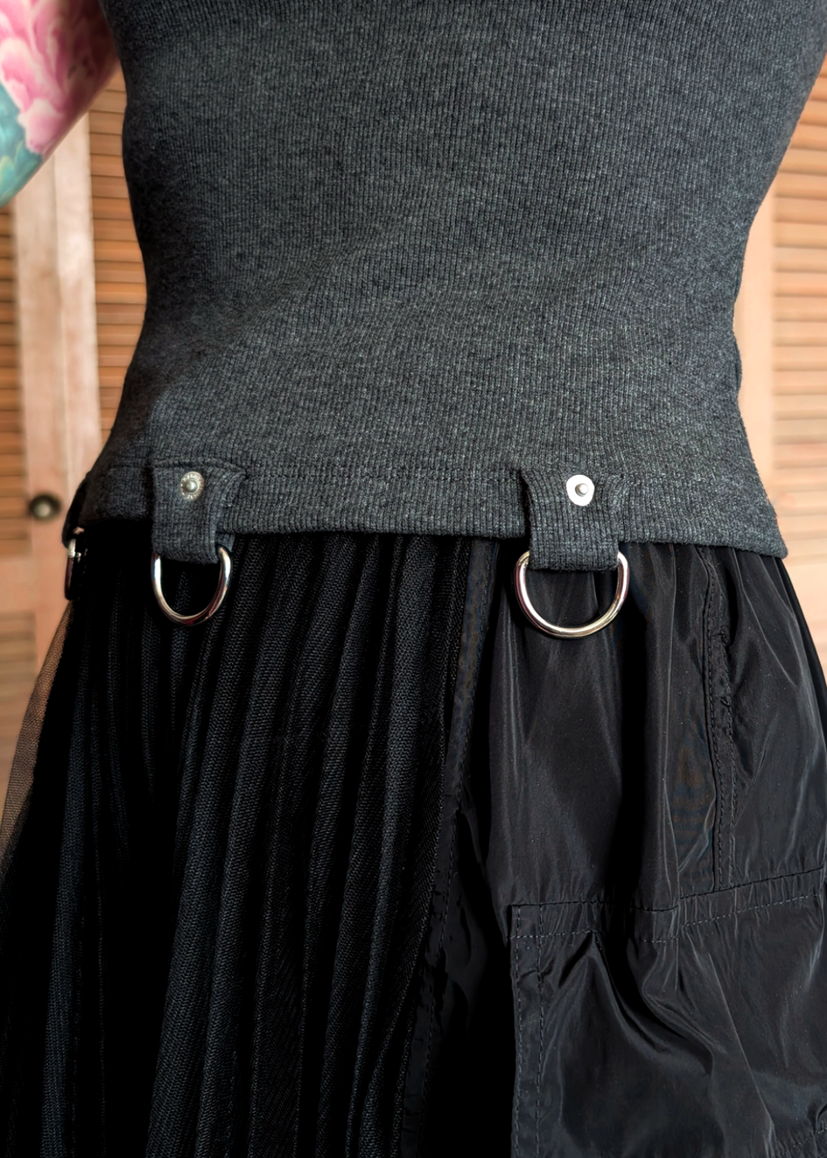 Person wearing a ribbed charcoal grey t-shirt with D-ring details at hem, and black skirt standing indoors.