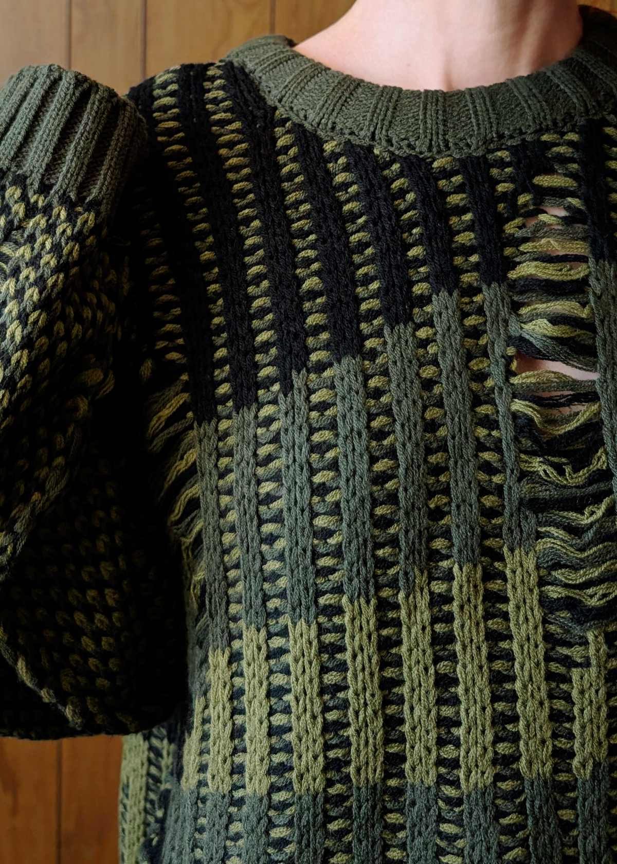 Close-up of a green and black patterned sweater with wooden panel background