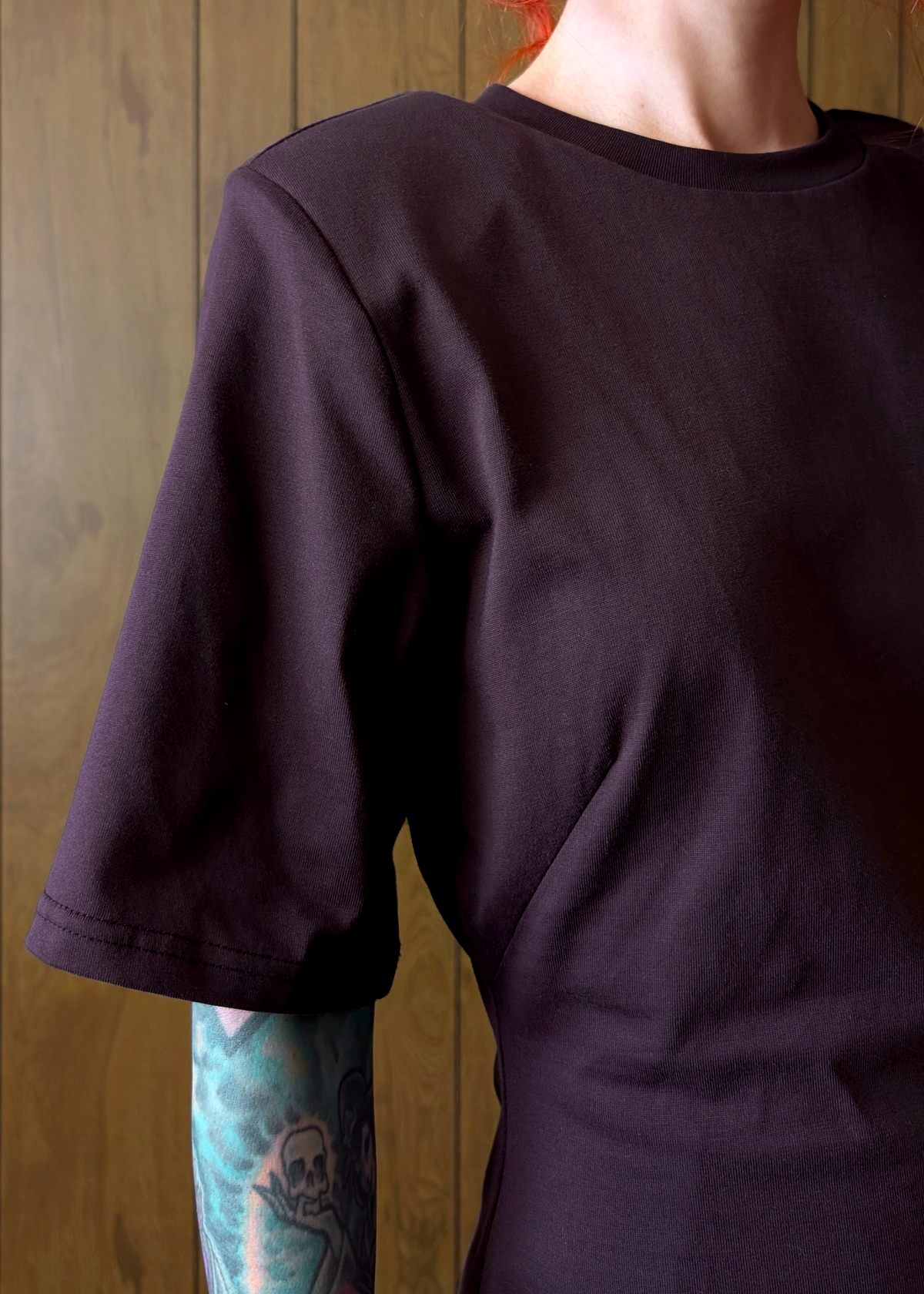 Person wearing a dark purple t-shirt dress with a wooden background