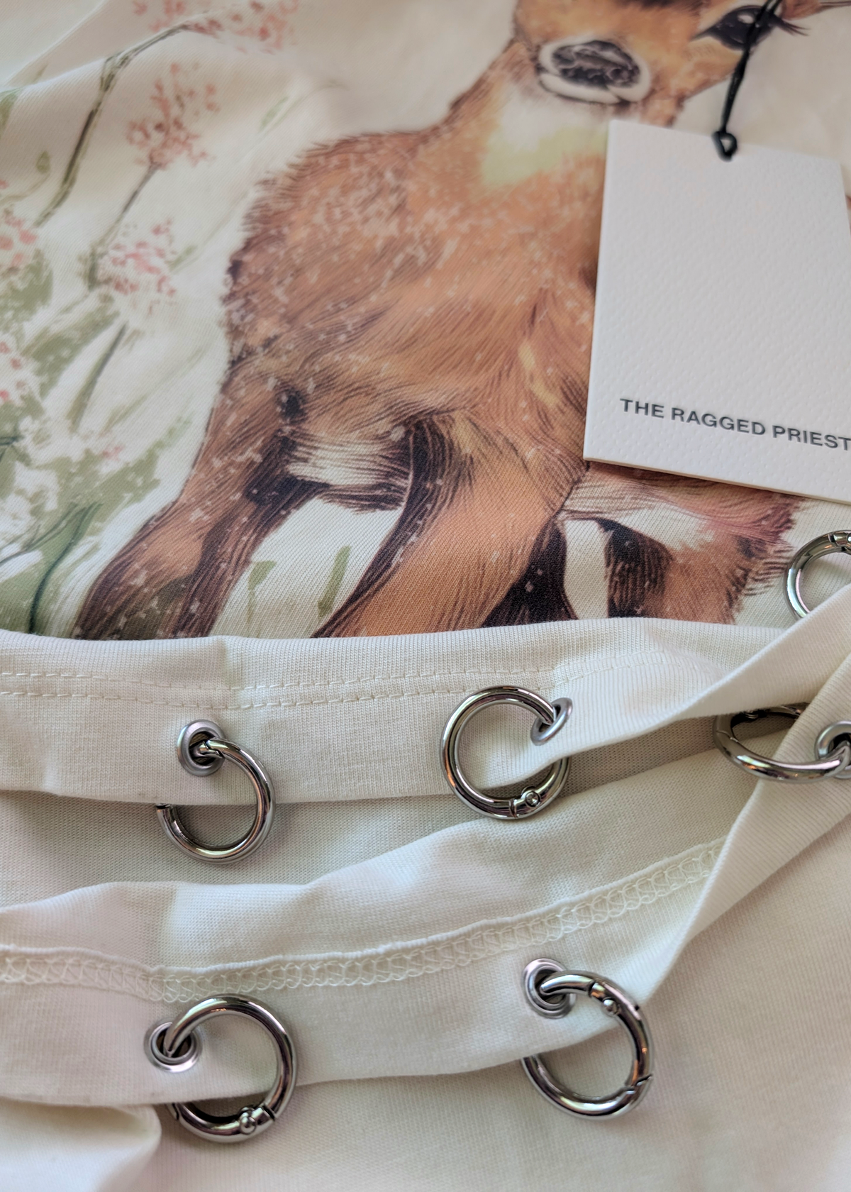Details of the silver O-rings along the hem of the ivory-colored graphic t-shirt with deer design