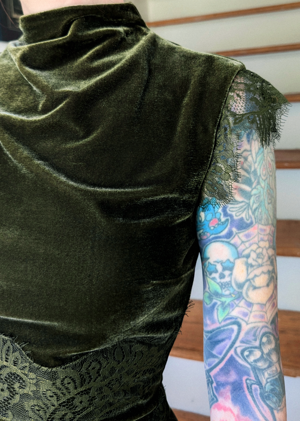 Close-up of a person wearing a dark olive green velvet sleeveless dress with lace trimmed cap sleeves