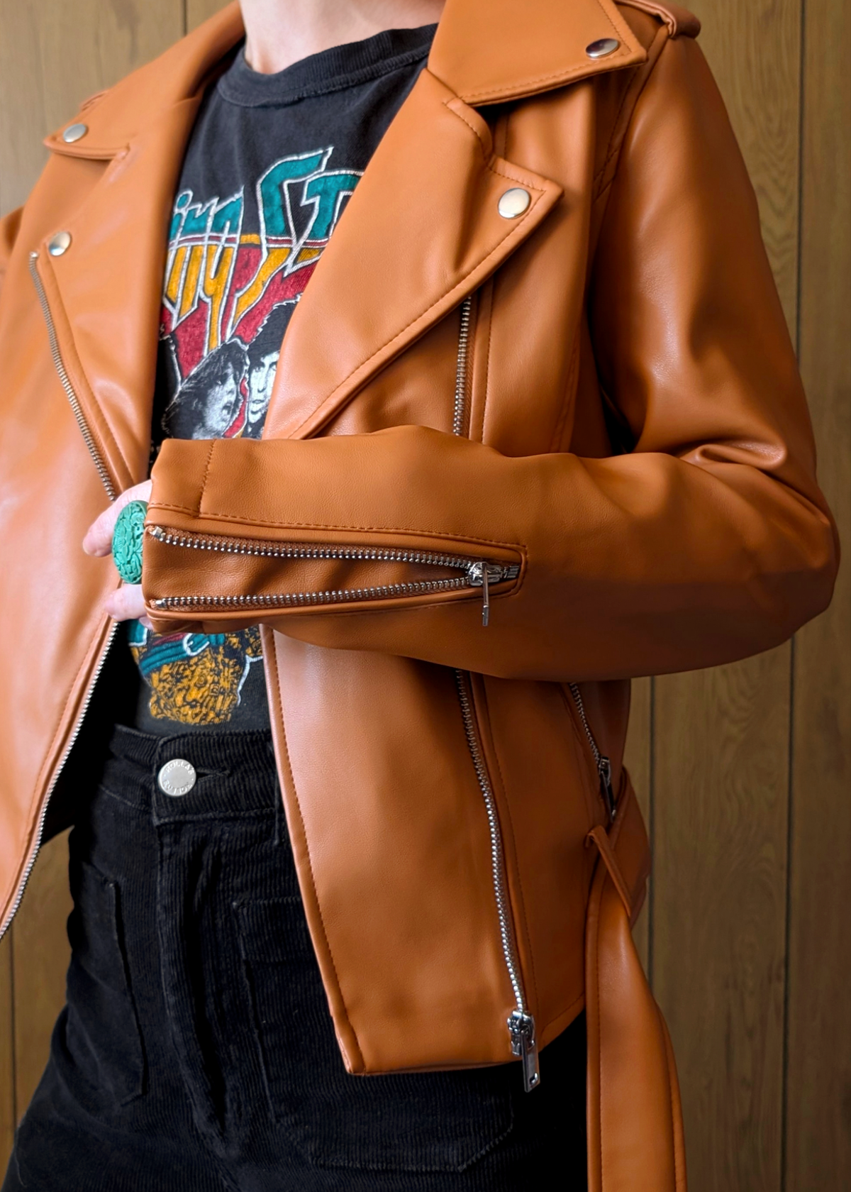 Person wearing an orange faux eather jacket over a colorful graphic t-shirt against a wooden background