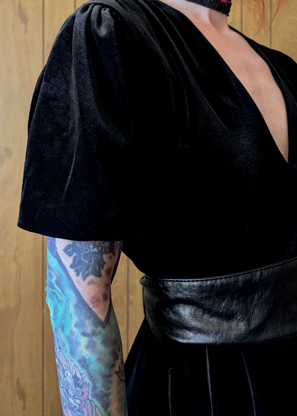 Person wearing a black velvet dress with short sleeves against a wooden background