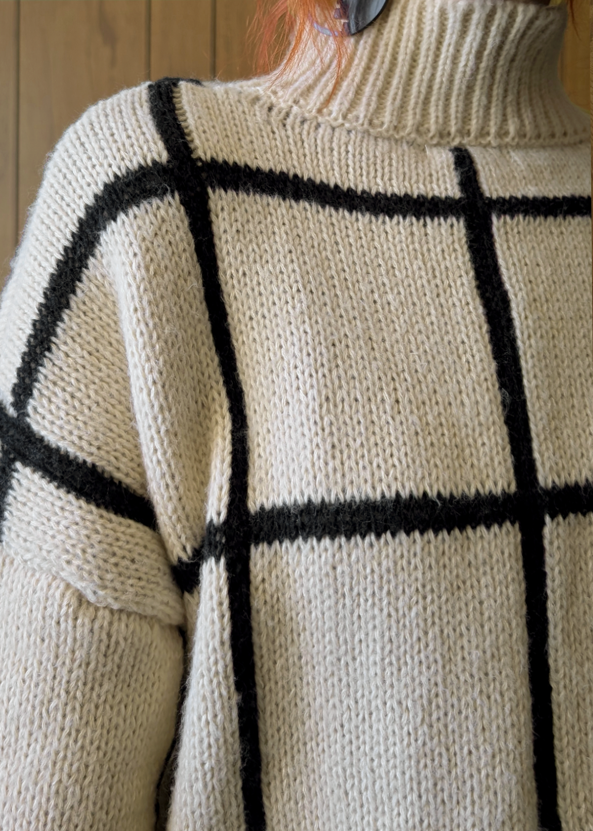 Close-up of a person wearing a beige sweater with black grid pattern.