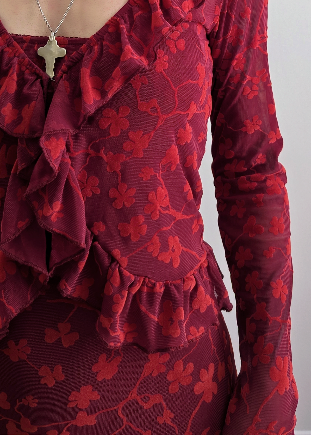 90s inspired burgundy red ruffled cardigan top made of a slinky mesh fabrication with flocked velvet floral design. Deep v-neckline, hook and eye closure at front. Long sleeves. By Motel Rocks