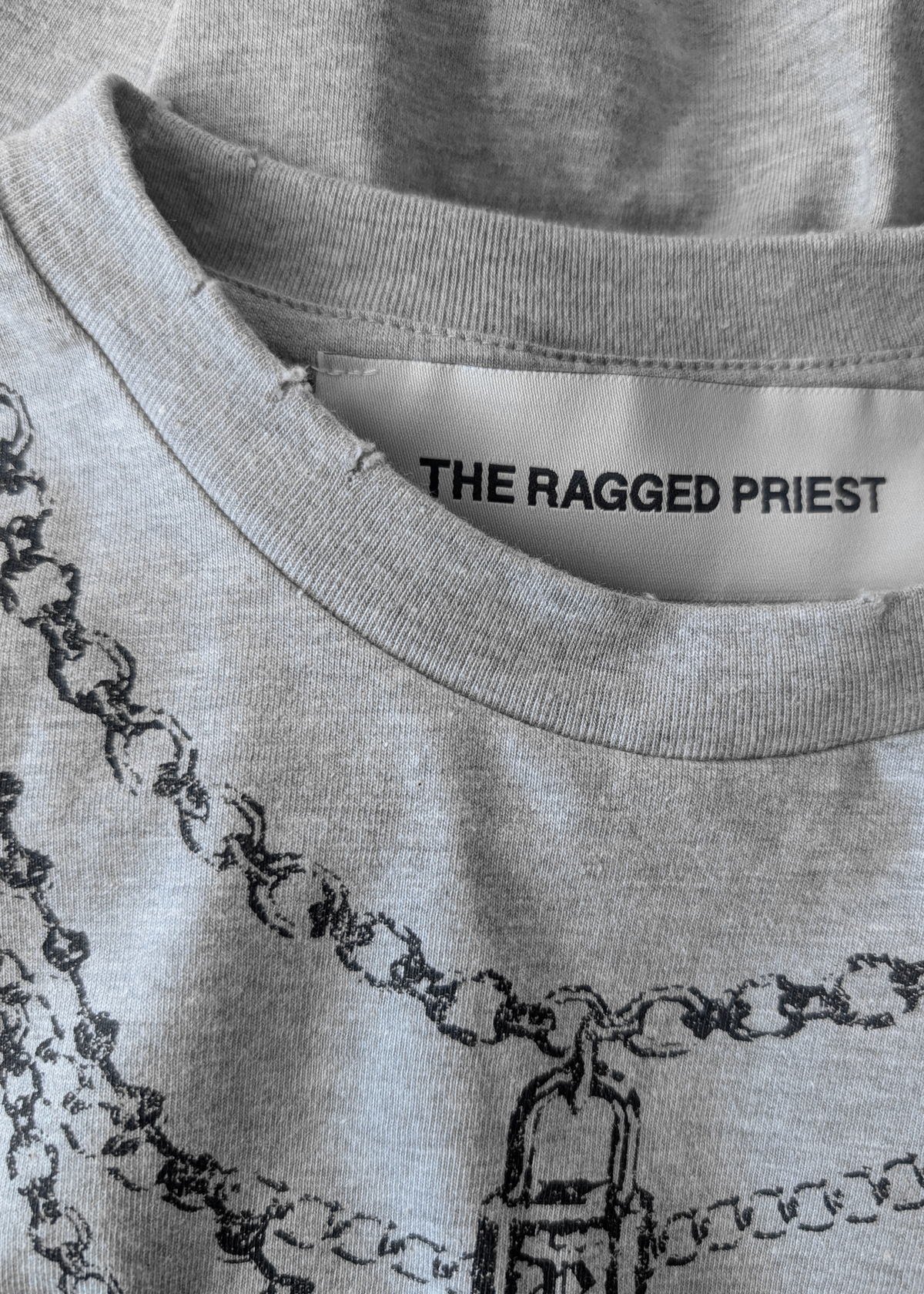 Details of the gray t-shirt with 'The Ragged Priest' tag and light destroyed, grinding details along neckline