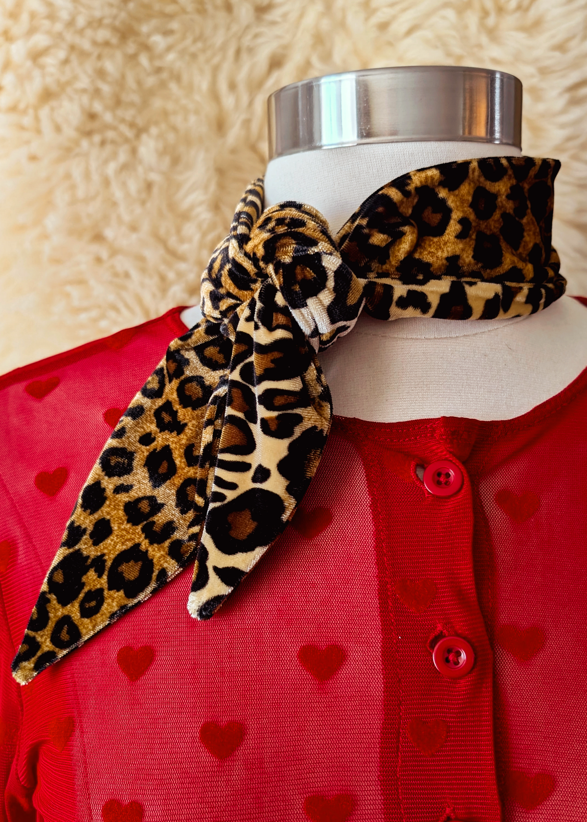 Mannequin wearing a red cardigan with heart patterns and a leopard print vevet scarf.