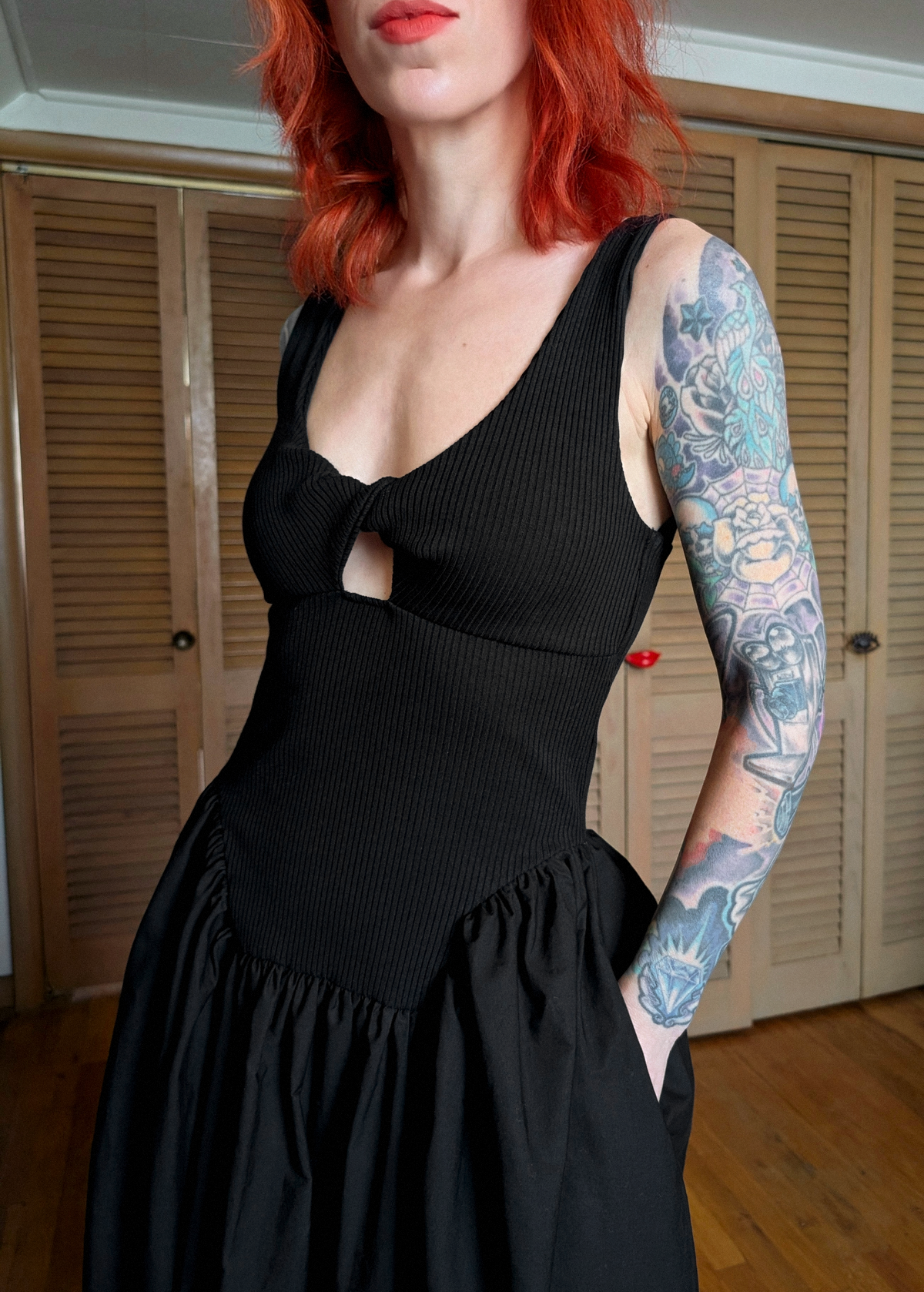 Person wearing a black dress standing in a room with wooden floors and shutters.
