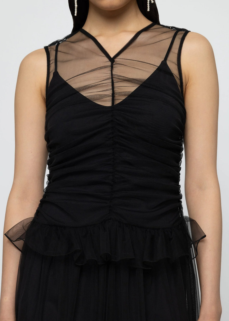 Black dress with sheer tulle and shirred details on a plain background