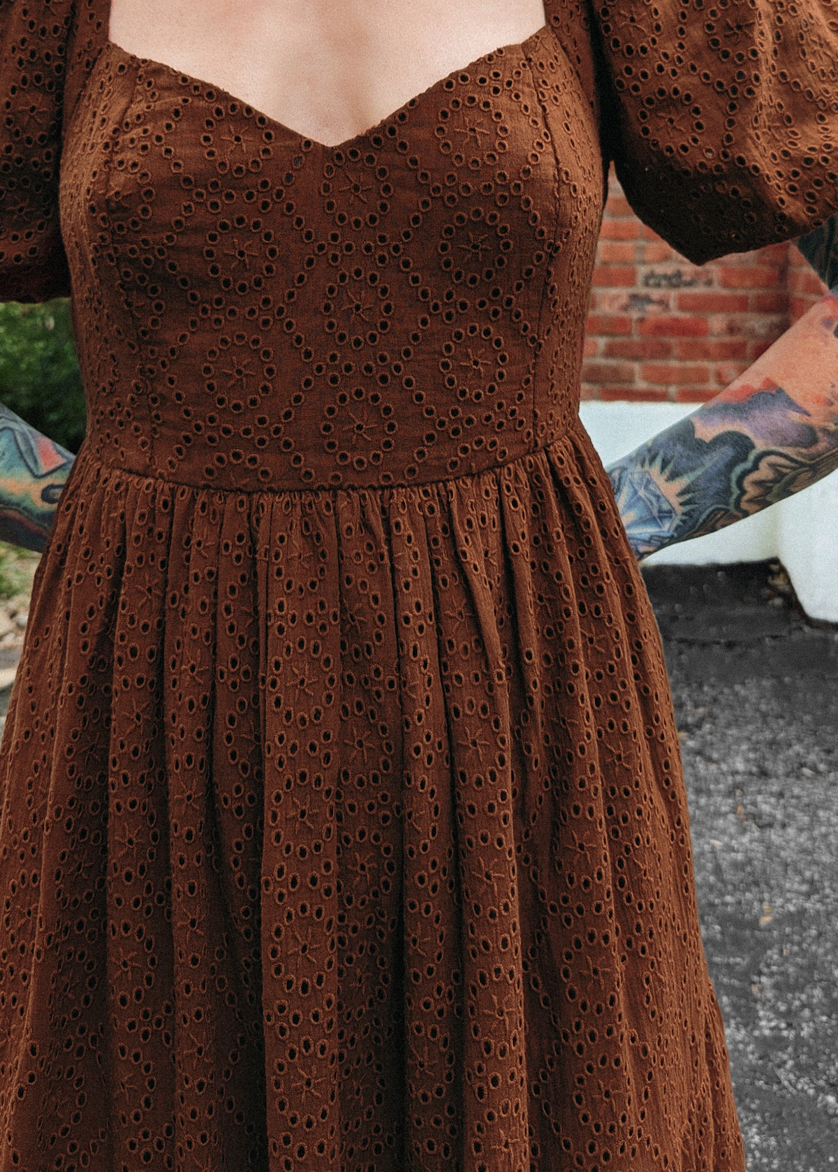 70s inspired prairie dress made of 100% eyelet cotton in a walnut brown colorway. Features puff sleeves, sweetheart neckline, smocked back with tie closure, and ruffled tiered skirt. 