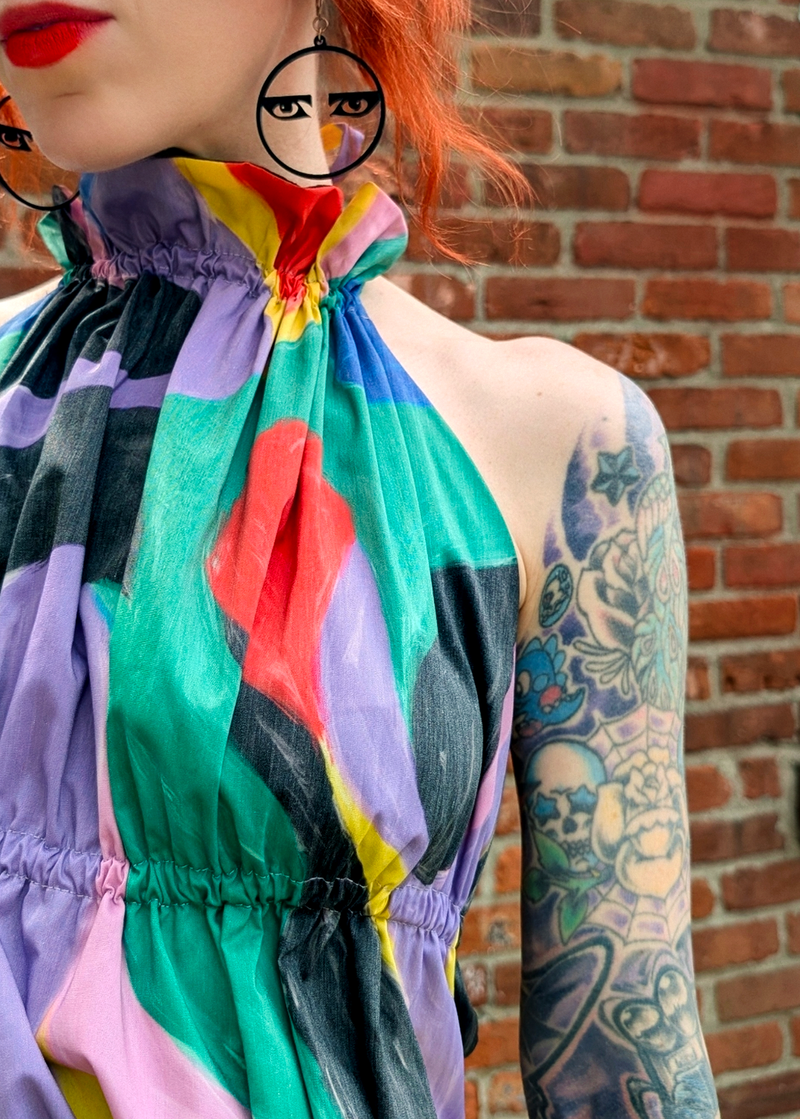Person wearing a colorful halter top standing against  a brick wall background