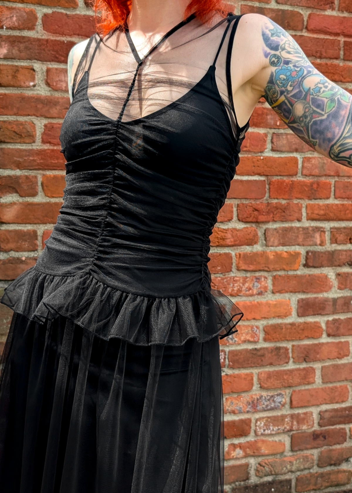 Person wearing a black tulle dress with sheer panels against a brick wall