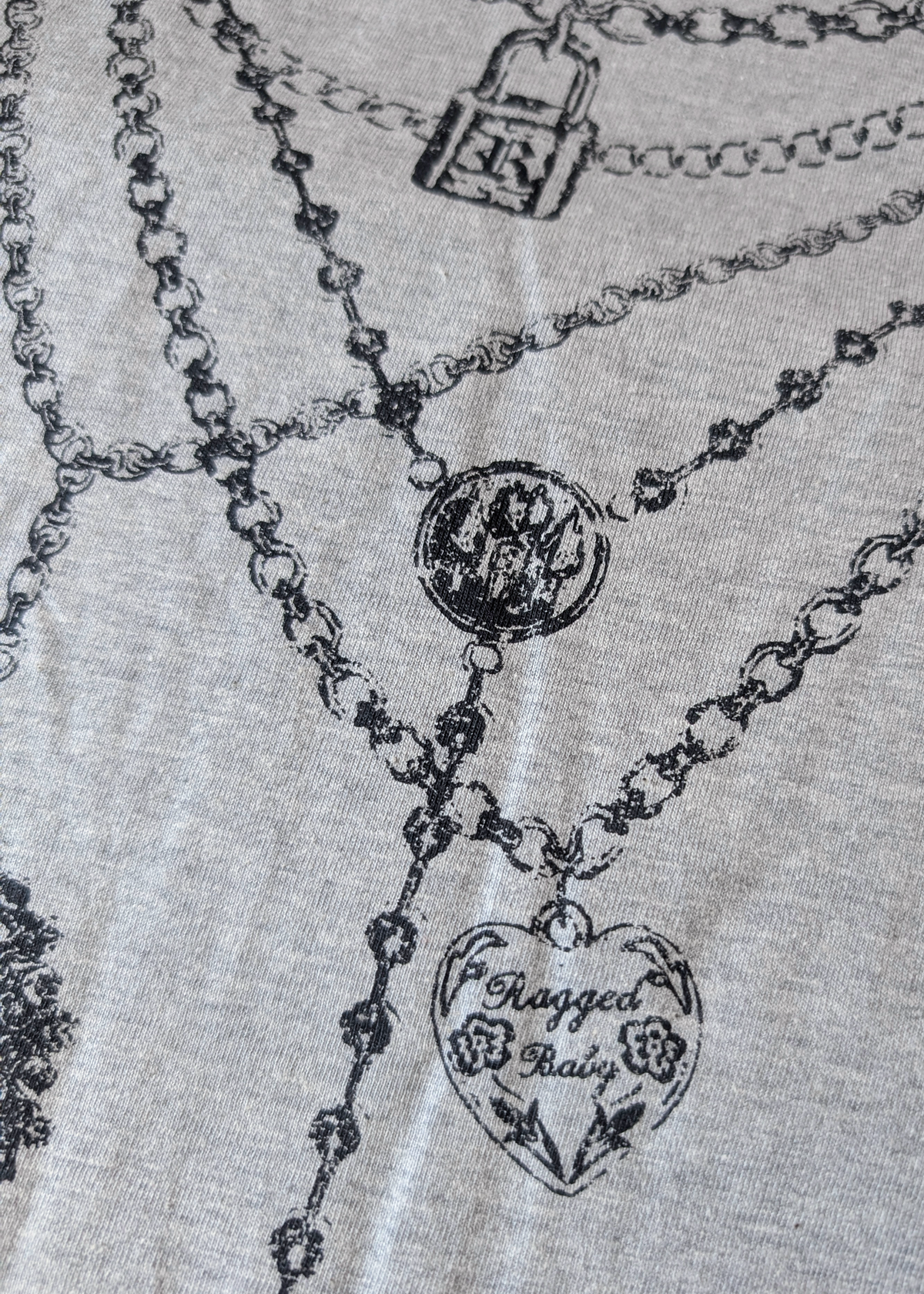 Detail of Necklace graphics on tee, featuring a heart-shaped pendant and lock charm and locket design in black