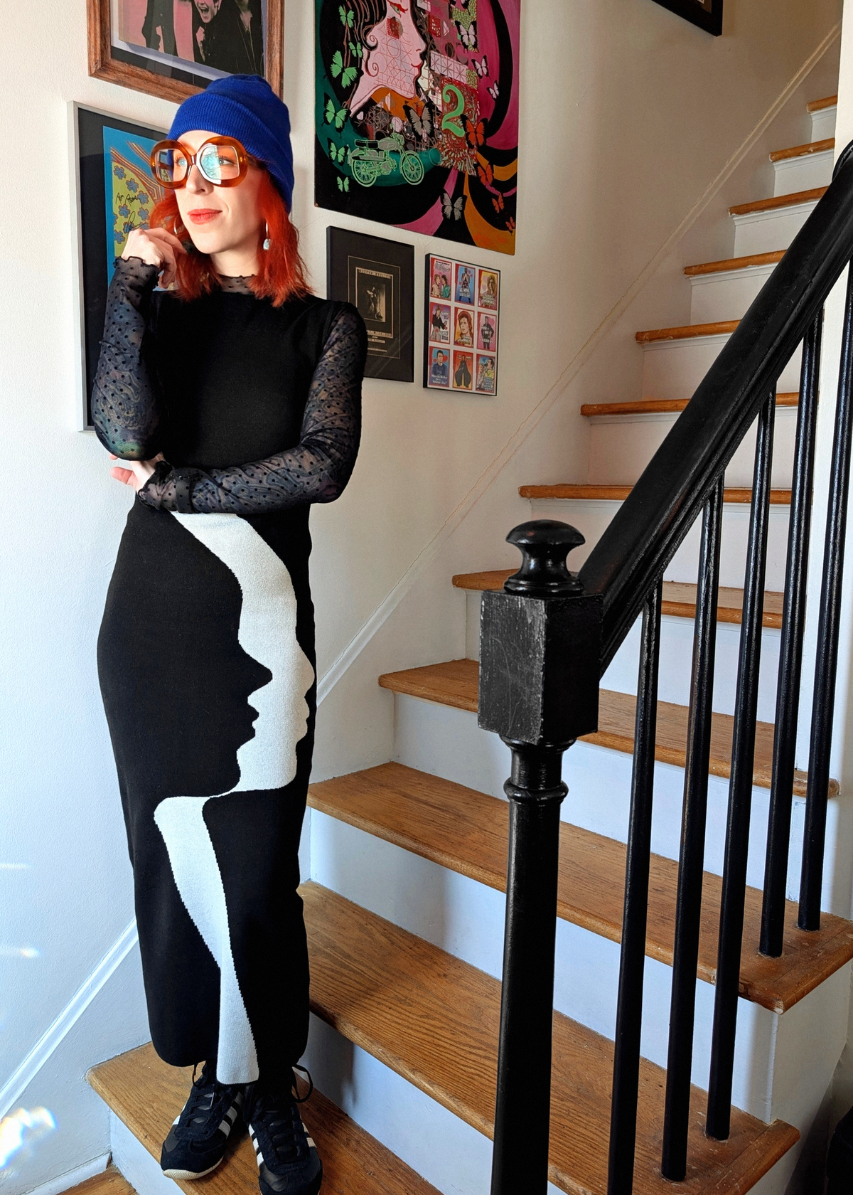 Person wearing a black and white knit dress with a face design, standing on a staircase.