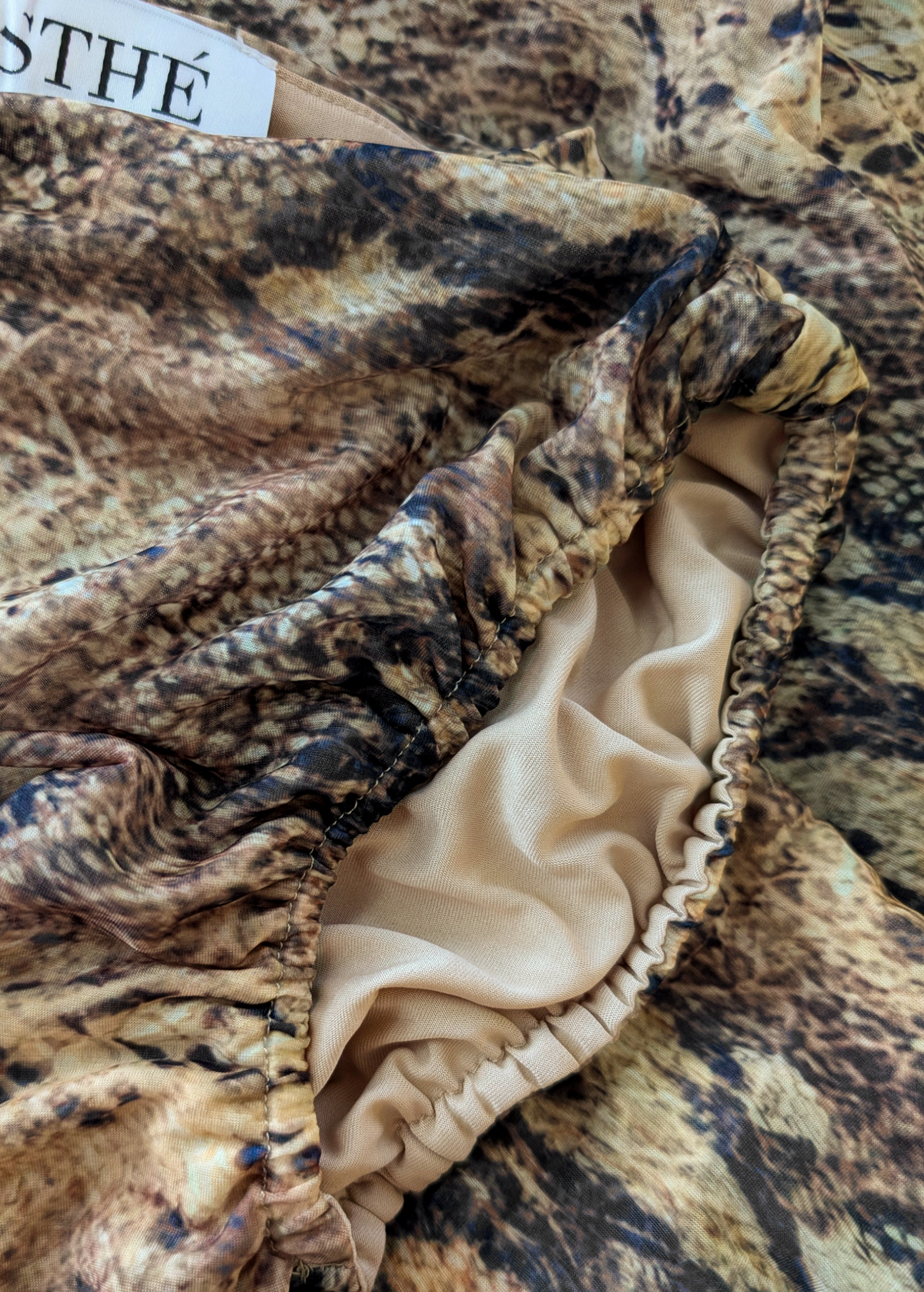 Close-up of snakeskin patterned fabric with a beige trim, brand name visible.