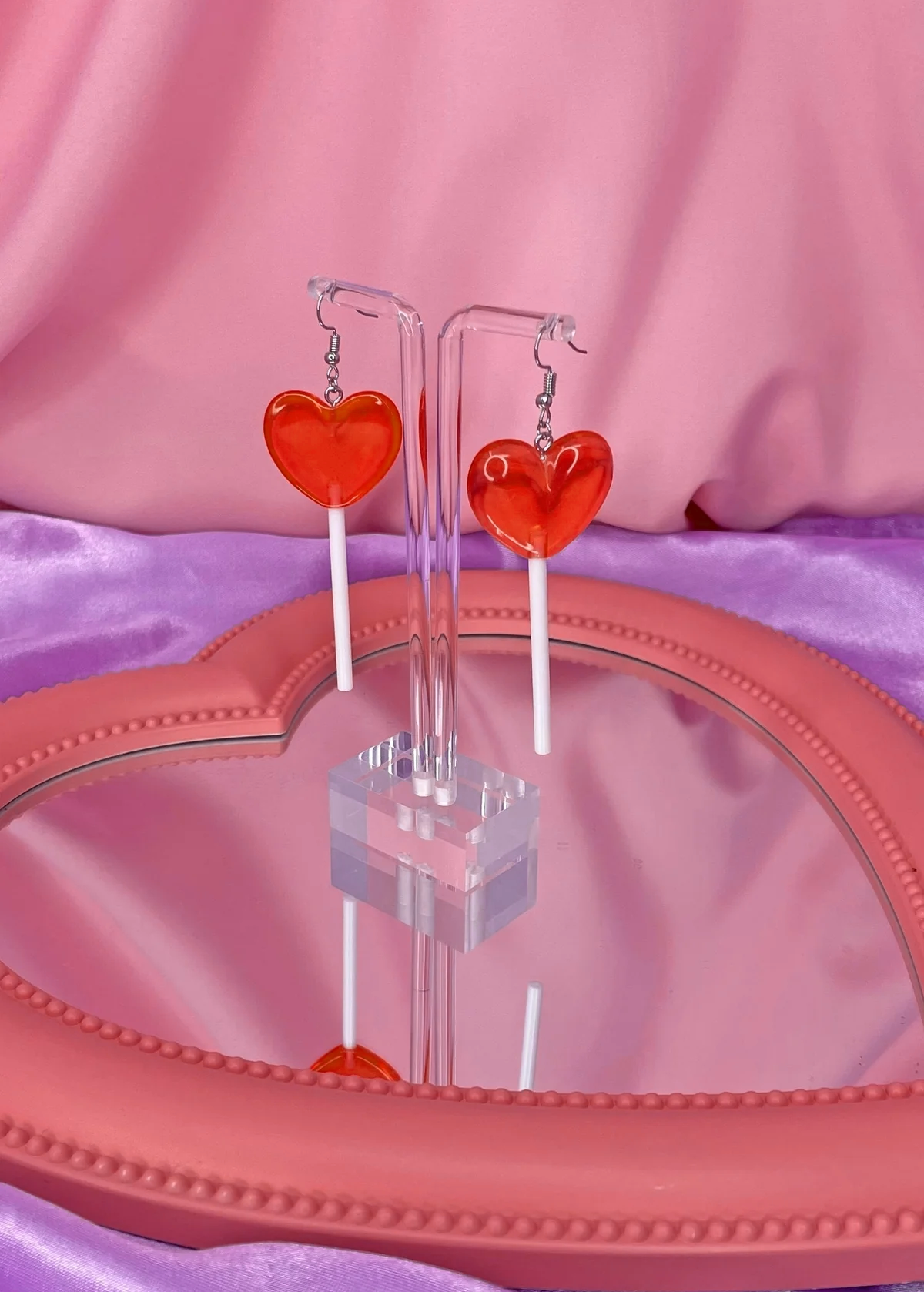 Red Heart-shaped earrings on a clear stand against a pink background