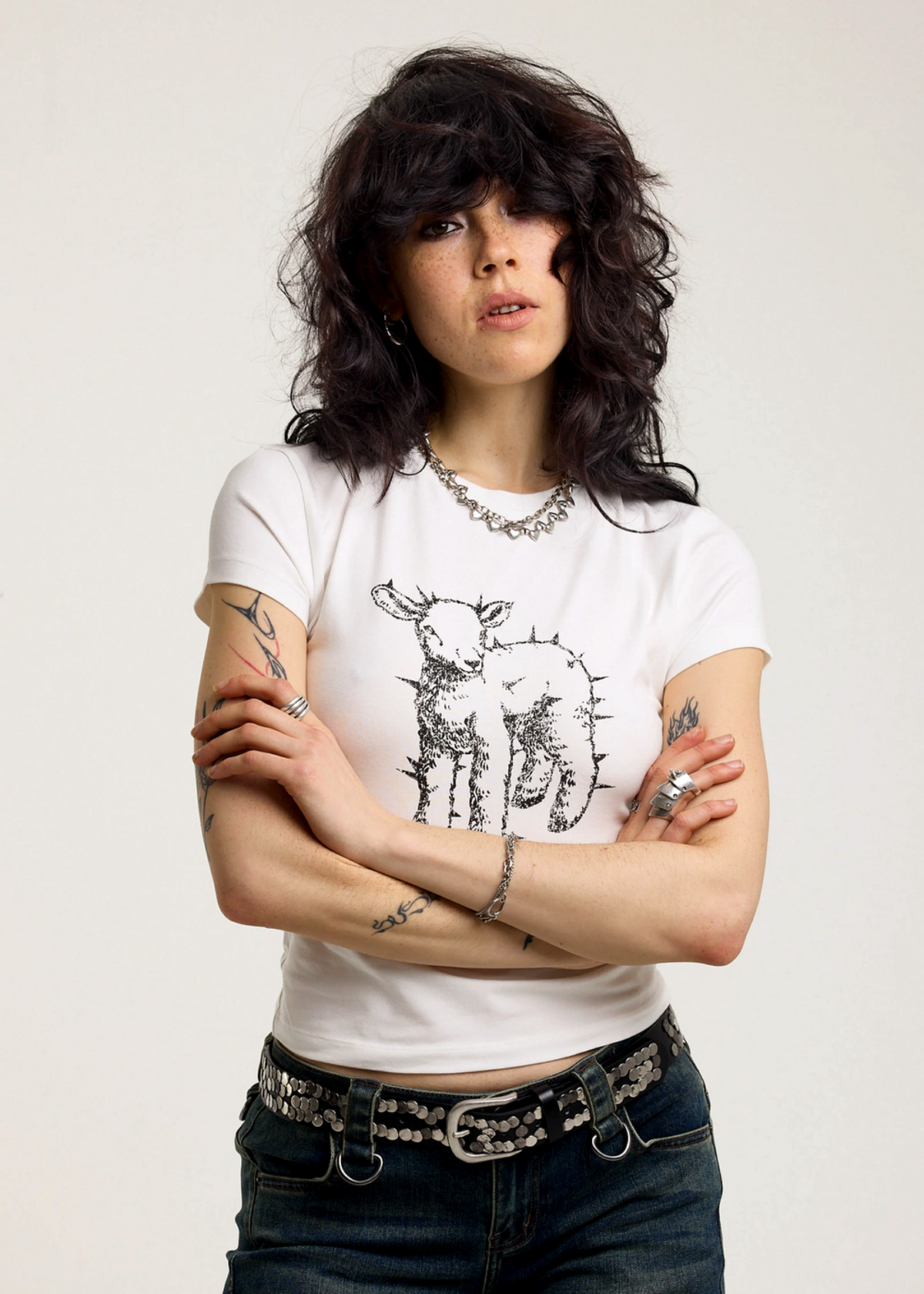 Person wearing an ivory t-shirt with a black spiked lamb graphic design on a plain background