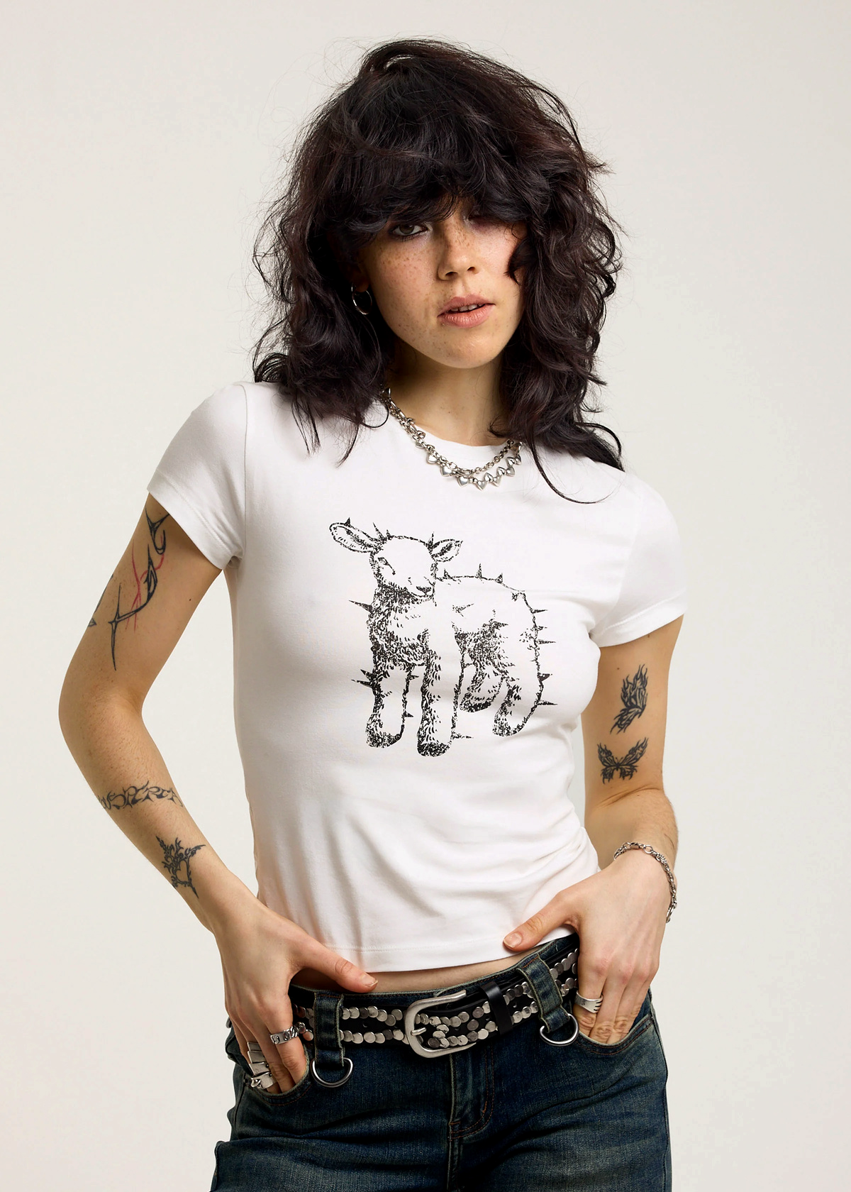 Woman wearing an ivory t-shirt with a black graphic design of a spiked lamb on a plain background