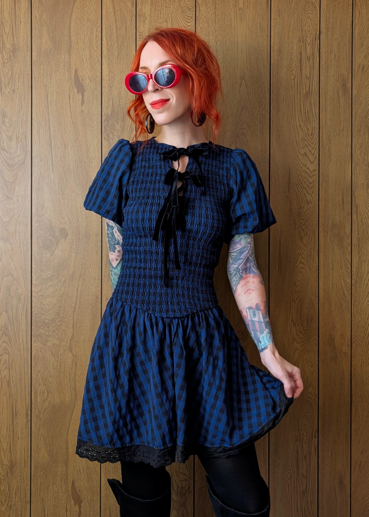 Woman wearing a navy and black checkered dress with puffed sleeves against a wooden background