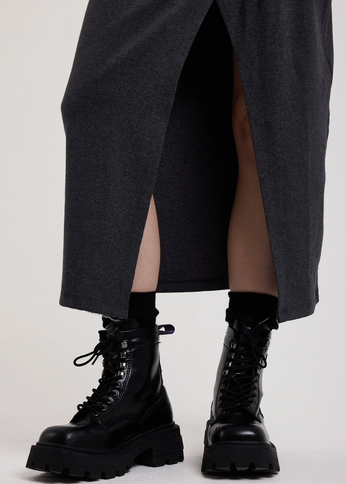 Person wearing black combat boots and a charcoal grey dress on a white background