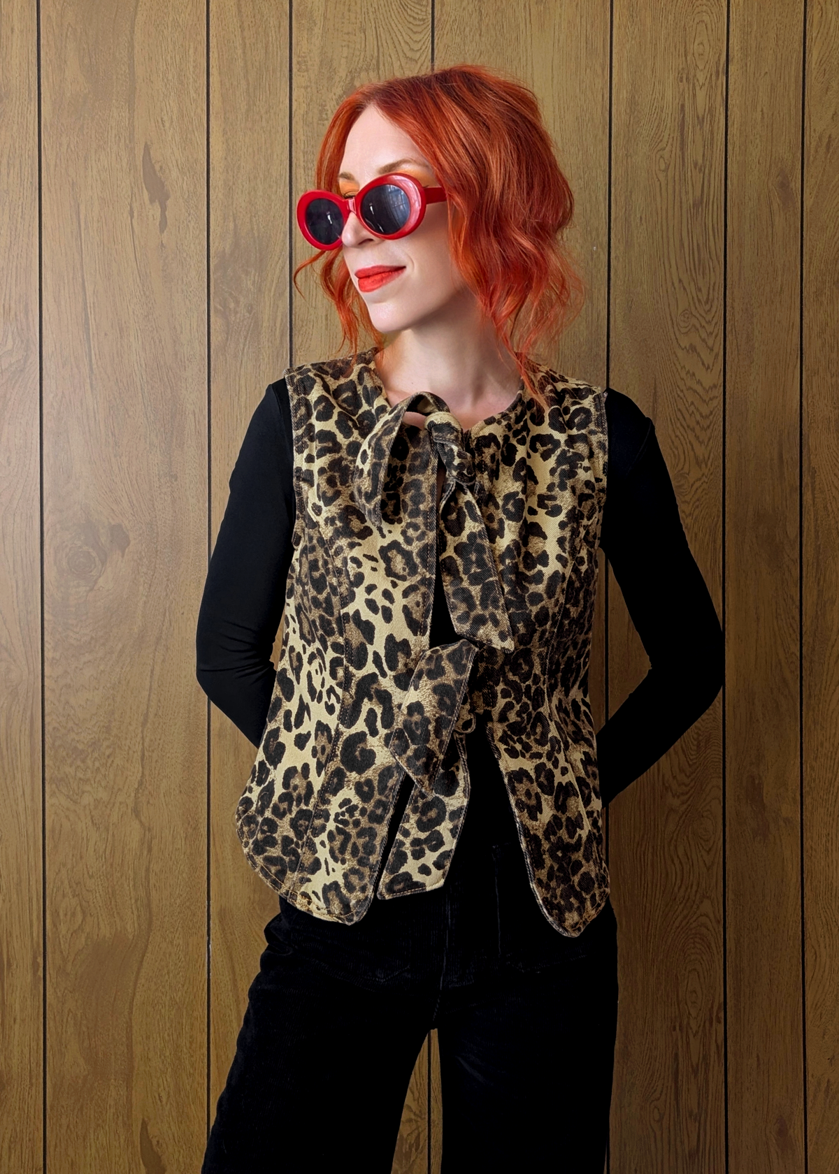 Person wearing a leopard print vest and red sunglasses against a wooden background