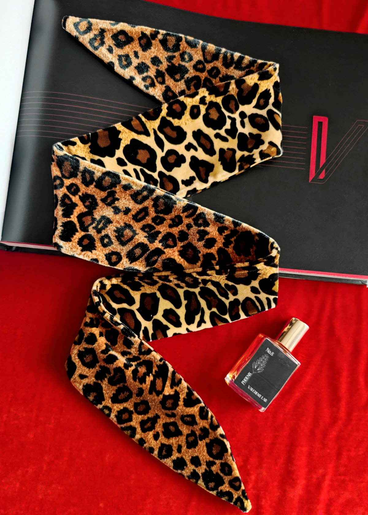 Leopard print velvet scarf on a black and red background with a perfume bottle.
