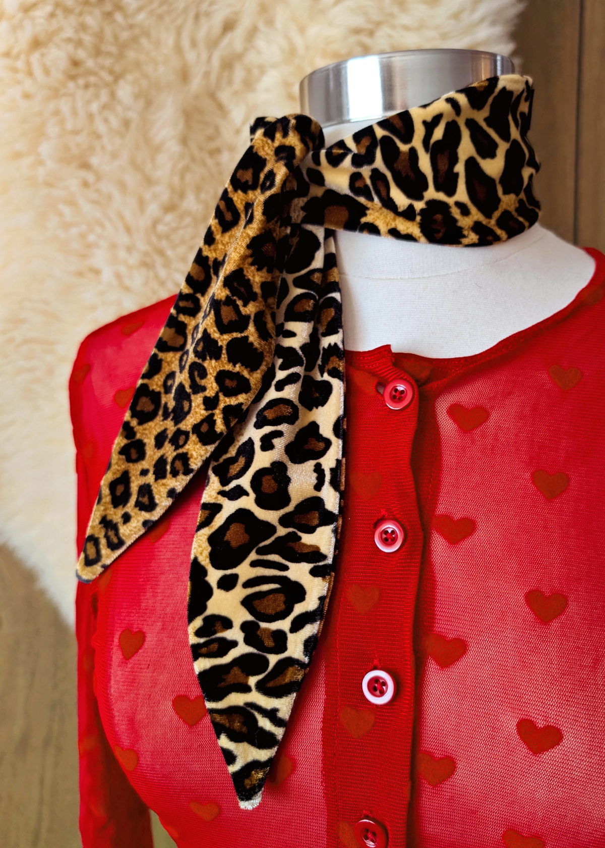 Mannequin wearing a red cardigan with heart patterns and a leopard print vevet scarf.