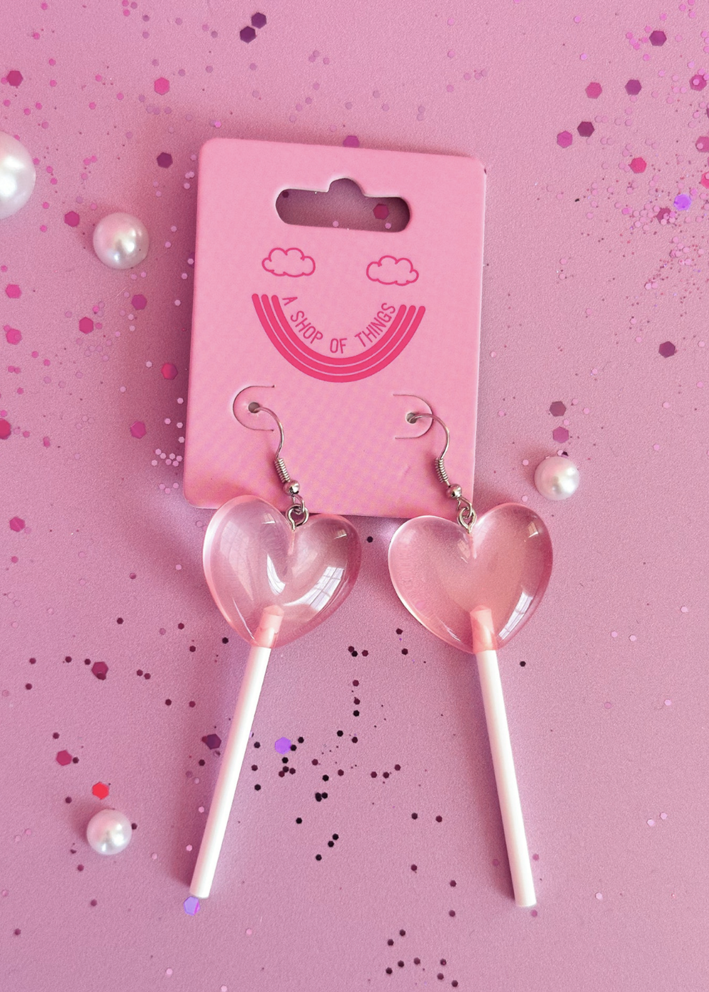 Heart-shaped lollipop earrings on a pink background with a branded card.